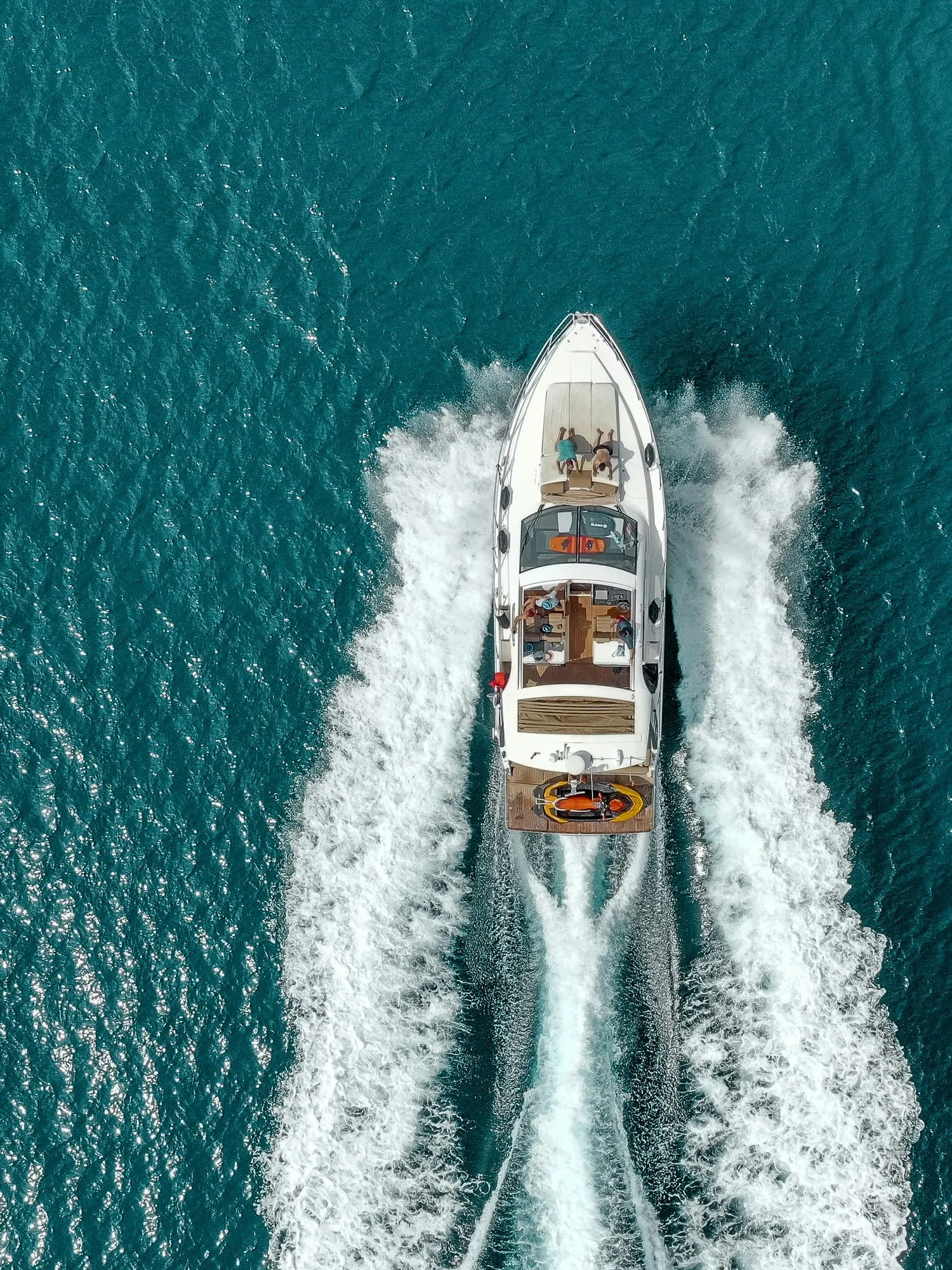 A yacht seen from above, cutting through blue-green water and leaving a white wake